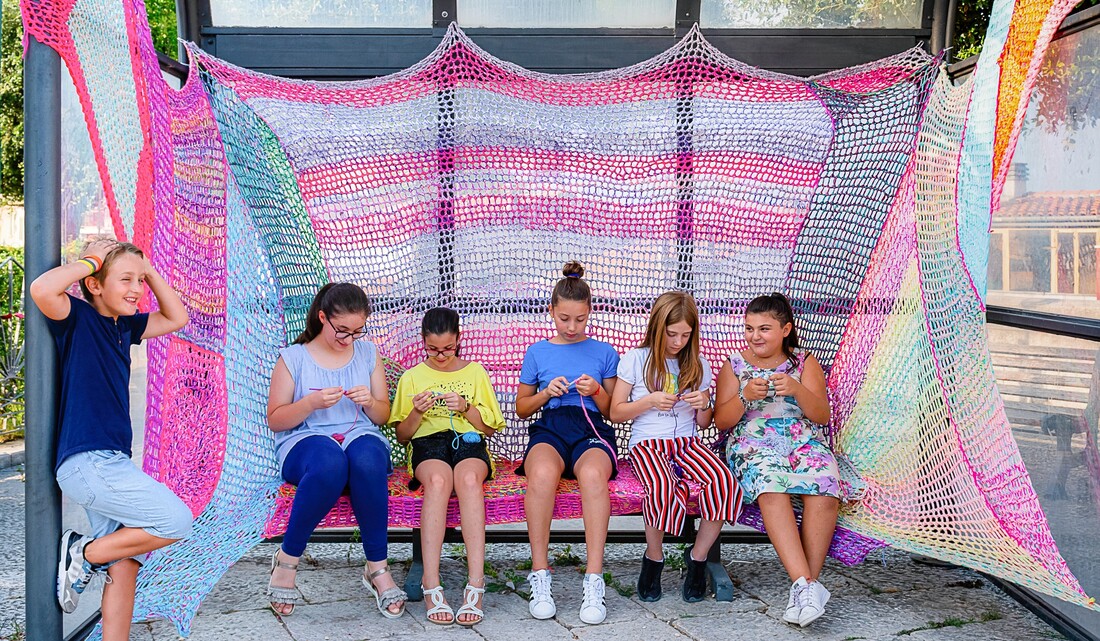 Children crocheting in yarnbombed bus stop created by Nicole Nikolich, Lace in the Moon, in Trivento, Italy for National Yarnbombing Day.